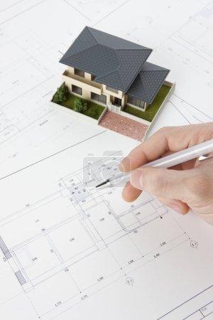 Photo for Architect holding pen with house model on desk, close-up view - Royalty Free Image