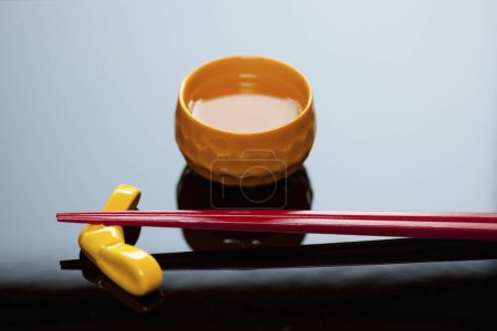 Téléchargez les photos : Vue rapprochée des baguettes placées sur la base de repos et la tasse de saké - en image libre de droit