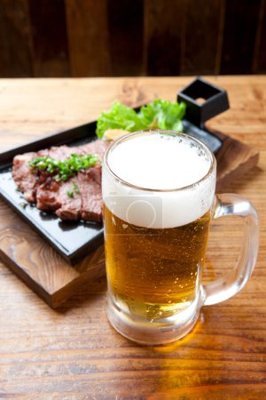 Foto de Una cerveza y un bistec sobre una mesa de madera - Imagen libre de derechos