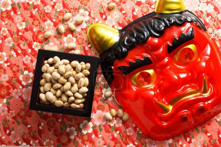 Photo for Devil mask and beans for mame-maki (bean-throwing) on table. Image of Setsubun, japanese traditional event. Setsubun means the day between two seasons. People throw beans to expel evil spirits and bring good luck - Royalty Free Image