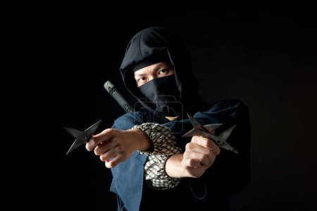 Photo for Young man in a ninja costume holding a pair of stars - Royalty Free Image
