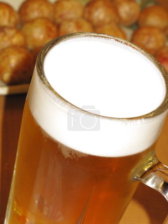 glass with beer with foam and food on background, close up