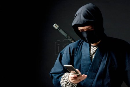 Photo for Young man in a ninja outfit holding a cell phone - Royalty Free Image