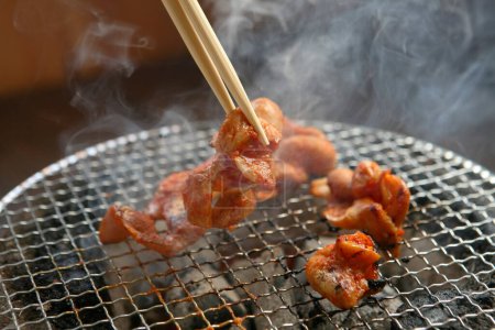Téléchargez les photos : Un gros plan de la friture de viande sur le gril avec des baguettes - en image libre de droit