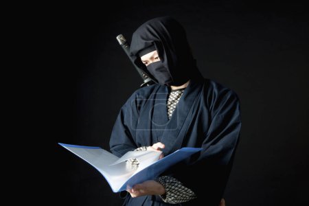 Téléchargez les photos : Jeune homme en tenue ninja tenant un livre bleu - en image libre de droit