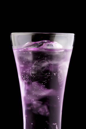 Téléchargez les photos : Gros plan d'un glaçon violet avec une éclaboussure d'eau sur un fond noir avec un verre. boire dans un verre d'eau. - en image libre de droit