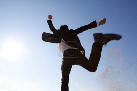 Foto de Hombre japonés en traje casual negro saltando al aire libre sobre fondo azul del cielo, vista inferior - Imagen libre de derechos