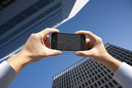 Téléchargez les photos : Plan recadré de la personne tenant smartphone avec écran blanc sur fond urbain - en image libre de droit