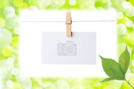 Foto de Hoja en blanco de papel colgando de la cuerda de la ropa, fondo borroso de verano verde con hojas - Imagen libre de derechos