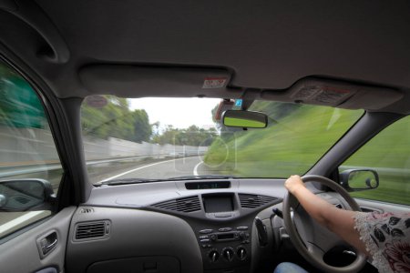 Téléchargez les photos : Jeune femme conduisant une voiture sur l'autoroute. Vue depuis les sièges arrière de la voiture. Road trip - en image libre de droit