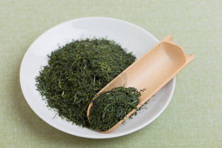 Téléchargez les photos : Feuilles de thé vert sec dans une assiette blanche et dans une cuillère en bois - en image libre de droit