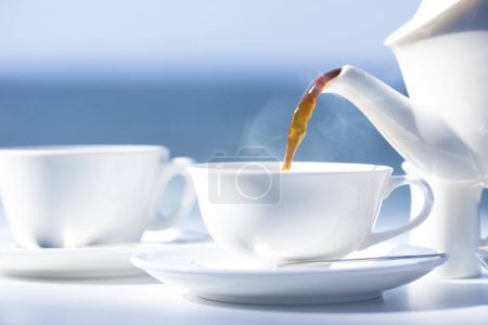 Foto de El té que vierte en la taza blanca sobre la mesa - Imagen libre de derechos