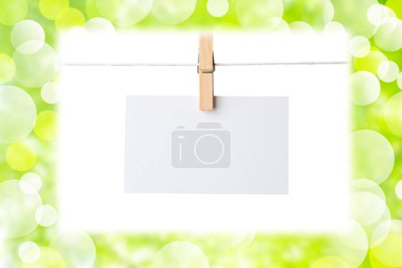Foto de Hoja en blanco de papel colgando de la cuerda de la ropa, fondo borroso de verano verde con hojas - Imagen libre de derechos