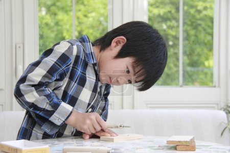 Photo for Preteen Asian boy playing with wooden blocks at home - Royalty Free Image