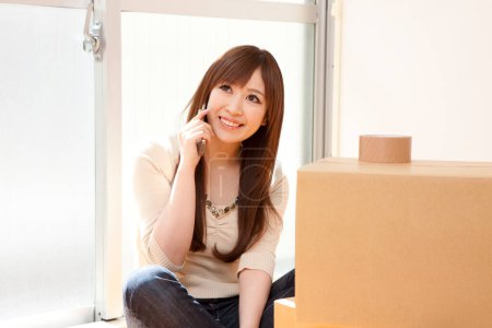 Photo for Asian woman talking on mobile phone with boxes - Royalty Free Image