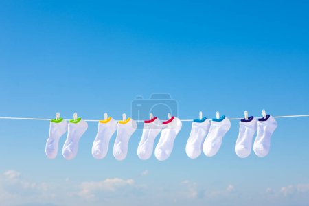 Téléchargez les photos : Chaussettes en coton blanc accrochées à la corde à linge contre le ciel bleu - en image libre de droit