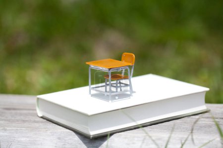 Téléchargez les photos : Jouet bureau d'école vide et chaise sur livre, objets miniatures sur herbe - en image libre de droit
