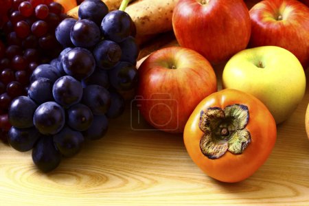 Foto de Surtido de caquis maduros, manzanas y uvas sobre mesa de madera - Imagen libre de derechos