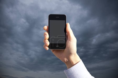 Téléchargez les photos : Plan recadré de la personne tenant smartphone avec écran blanc sur fond bleu ciel - en image libre de droit