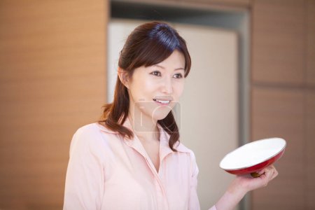 asian woman in kitchen holding pot lid