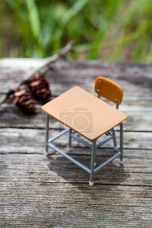 Téléchargez les photos : Jouet bureau d'école vide et chaise sur planche de bois dans le parc, objets miniatures sur herbe - en image libre de droit