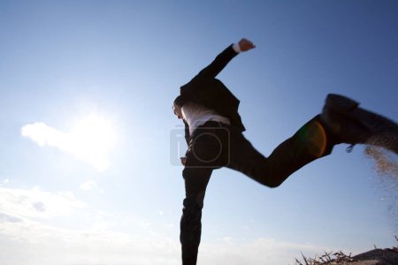 Téléchargez les photos : Japonais en costume décontracté noir sautant à l'extérieur sur fond bleu ciel, vue du bas - en image libre de droit