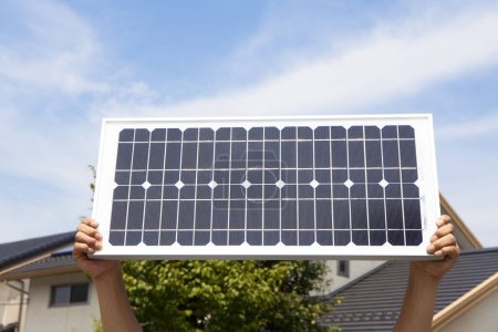 Téléchargez les photos : Mains tenant panneau d'énergie solaire sur ciel bleu - en image libre de droit