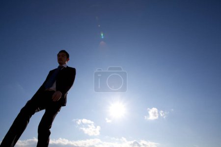 Téléchargez les photos : Japonais en costume décontracté noir debout à l'extérieur sur fond bleu ciel - en image libre de droit