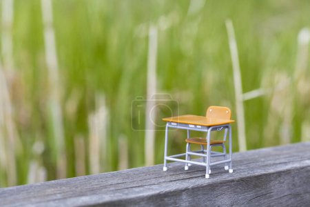 Téléchargez les photos : Jouet bureau d'école vide et chaise sur planche de bois dans le parc, objets miniatures sur herbe - en image libre de droit