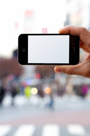 Foto de Captura recortada de la persona que sostiene el teléfono inteligente con pantalla en blanco en el fondo urbano - Imagen libre de derechos