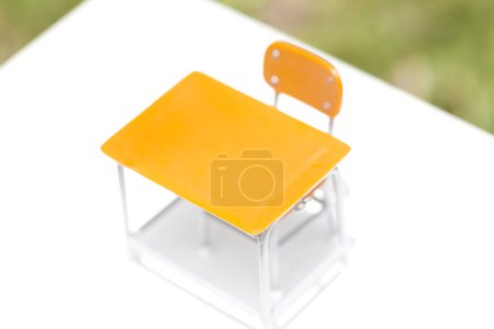 Téléchargez les photos : Jouet bureau d'école vide et chaise sur livre, objets miniatures sur herbe - en image libre de droit