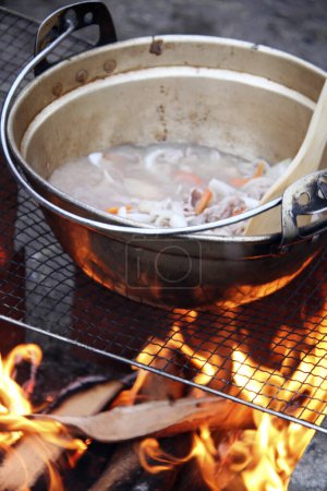 Foto de Preparando comida en el campamento - comida caliente hirviendo en la olla grande sobre el fuego - Imagen libre de derechos