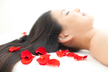 Photo for Beautiful asian woman with close eyes relax on bed with red rose petals in spa salon. - Royalty Free Image