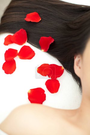 Téléchargez les photos : Belle asiatique femme couché sur lit avec rouge rose pétales dans spa salon. - en image libre de droit