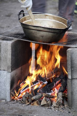 Foto de Preparando comida en el campamento - comida caliente hirviendo en la olla grande sobre el fuego - Imagen libre de derechos