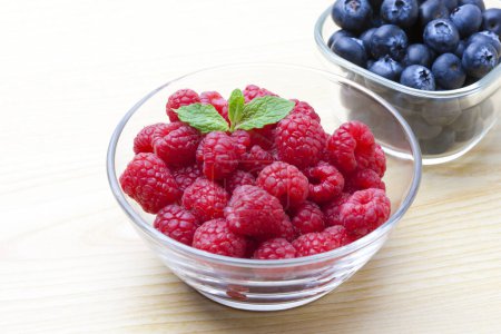 Photo for Fresh ripe blueberries and raspberries in bowls on wooden background - Royalty Free Image
