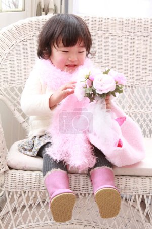 Photo for Cute Asian little girl wearing pink scarf holding bouquet of roses at home - Royalty Free Image
