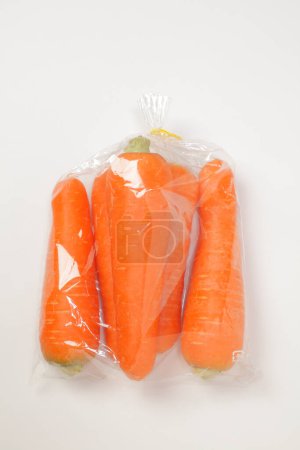 Foto de Bolsa de plástico con zanahorias frescas en blanco - Imagen libre de derechos