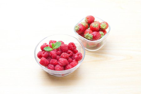 Photo for Fresh raspberries and strawberries in transparent bowls on wooden table background. - Royalty Free Image