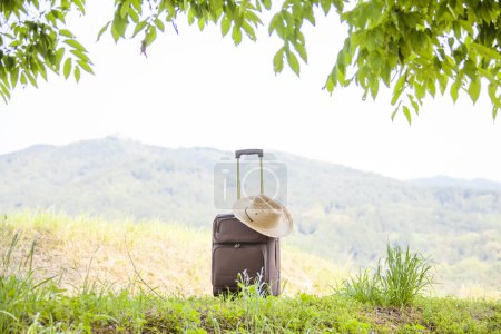 Téléchargez les photos : Valise avec chapeau de paille et veste contre paysage de montagne, concept de voyage et de tourisme - en image libre de droit