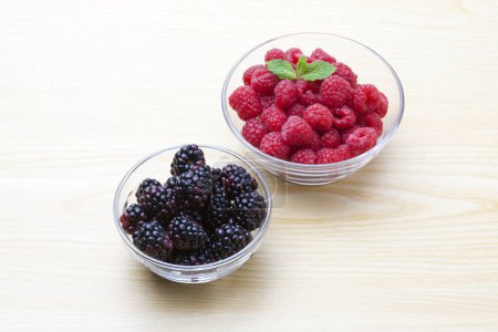 Photo for Fresh raspberries and blackberries in bowls on wooden table - Royalty Free Image