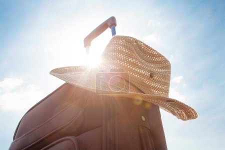 Foto de Maleta con sombrero de paja contra el cielo azul, viaje y concepto de vacaciones. - Imagen libre de derechos