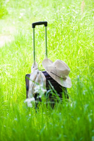 Foto de Maleta con sombrero de paja sobre hierba verde, concepto de viaje - Imagen libre de derechos