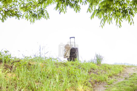 Téléchargez les photos : Valise avec chapeau de paille sur herbe verte, concept de voyage - en image libre de droit