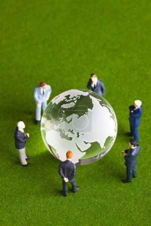 Téléchargez les photos : Hommes d'affaires miniatures avec globe en verre debout sur la surface verte - en image libre de droit