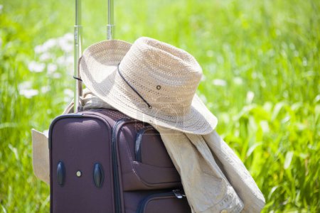 Foto de Maleta con sombrero de paja sobre hierba verde, concepto de viaje - Imagen libre de derechos