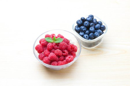 Photo for Fresh ripe blueberries and raspberries in bowls on wooden background - Royalty Free Image