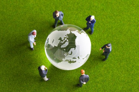 Téléchargez les photos : Hommes d'affaires miniatures avec globe en verre debout sur la surface verte. concept d'entreprise internationale - en image libre de droit