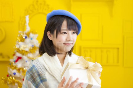 Photo for Portrait of beautiful young japanese woman holding gift box on yellow wall background with christmas tree - Royalty Free Image