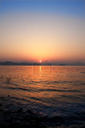 Téléchargez les photos : Magnifique coucher de soleil sur le lac avec des collines à l'horizon - en image libre de droit